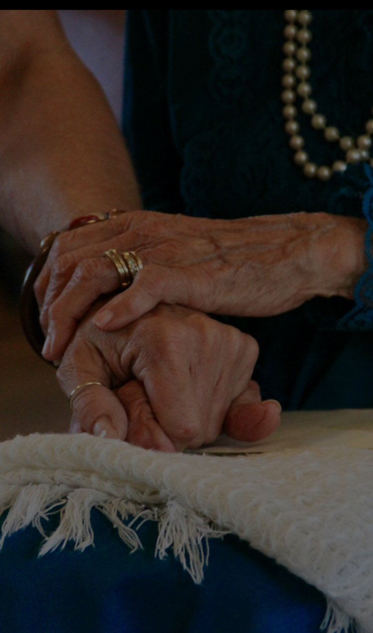 An elderly woman holds the hand of a younger woman in her lap.